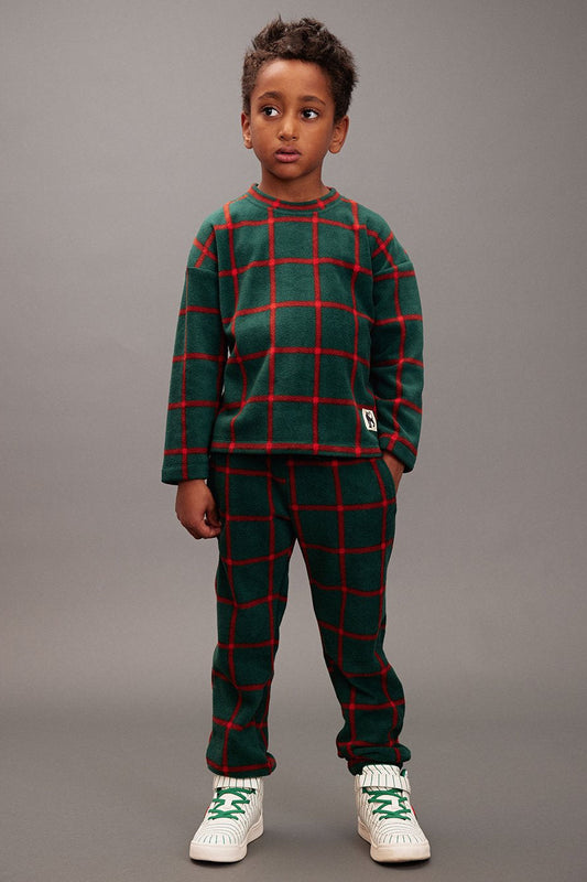 Child wearing a green and red plaid outfit with white sneakers on a gray background