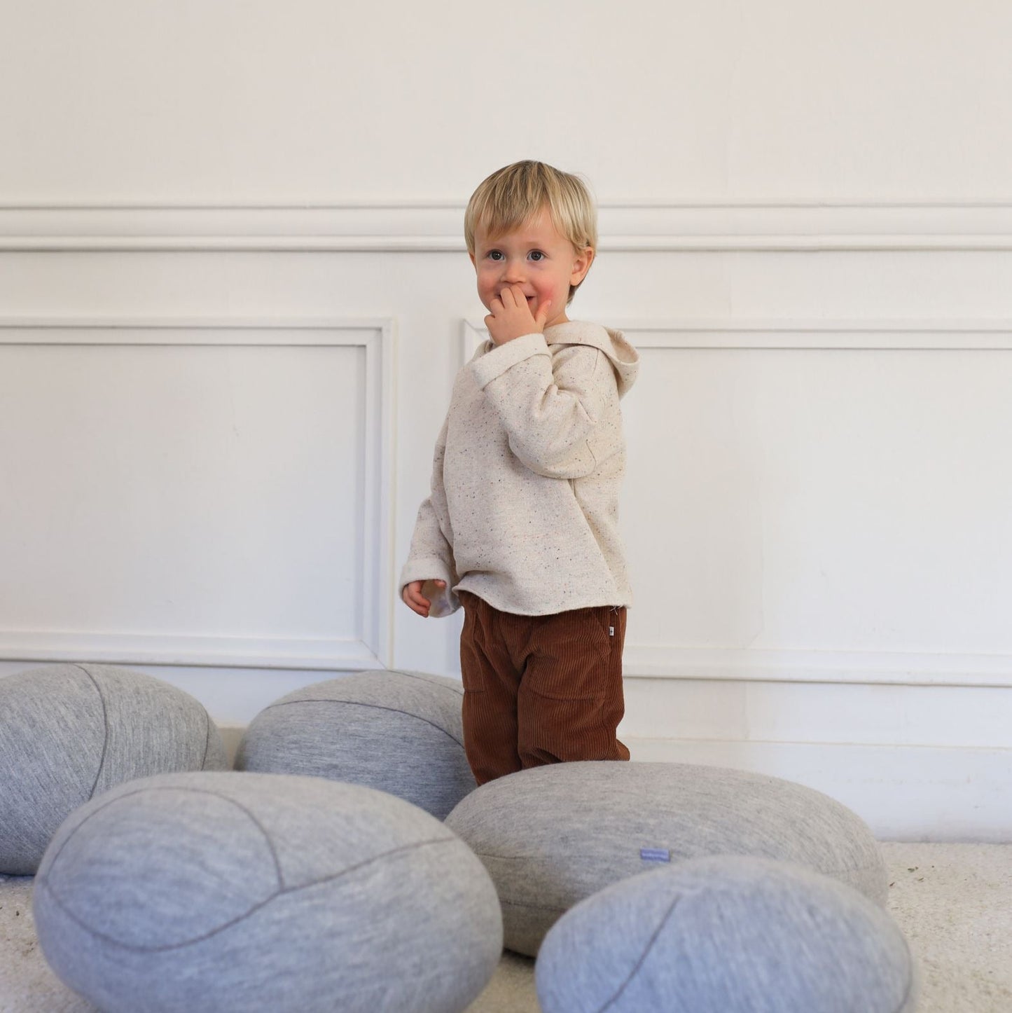 Child standing among gray bean bags against a white wall