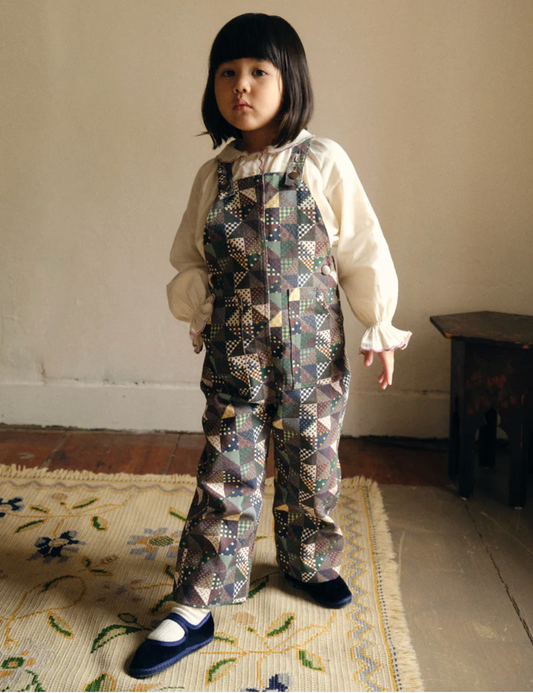 Child wearing a patterned outfit standing on a rug with a neutral background